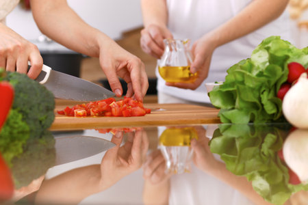 Closeup of human hands cooking in kitchen. Mother and daughter or two female friends cutting vegetables for fresh salad. Healthy meal, vegetarian food and lifestyle conceptsの写真素材
