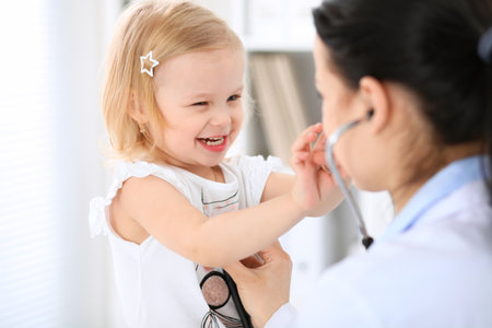 Doctor and patient baby in hospital. Little girl is being examined by pediatrician with stethoscope. Health care, insurance and help conceptの写真素材