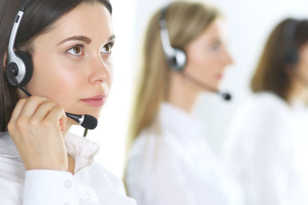 Group of call center operators at work. Focus at beautiful business woman in headsetの写真素材