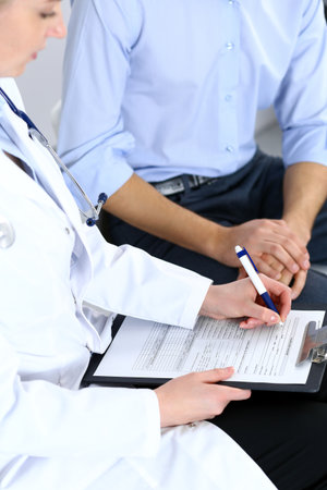 Female doctor holding application form while consulting man patient in hospital. Medicine and healthcare conceptの写真素材