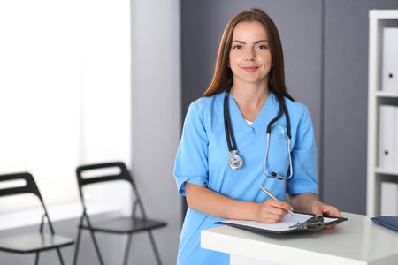 Doctor woman at work. Portrait of female physician filling up medical form while standing near reception desk at clinic or emergency hospital. Medicine and healthcare conceptの写真素材