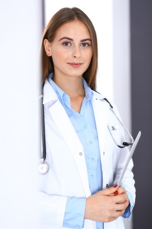 Doctor woman using tablet computer while standing straight near window in hospital. Happy physician at work. Medicine and health care conceptの写真素材