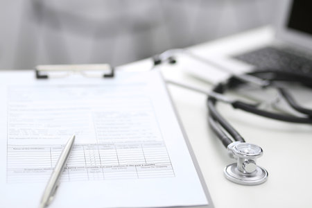 Stethoscope, clipboard with medical form lying on hospital reception desk with laptop computer. Medical tools at doctor working table.Medicine and health care concept.の写真素材