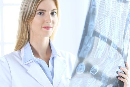 Doctor woman osteopathist examining x-ray picture while standing near window in clinic or hospital....