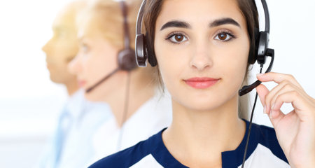 Call center operators at work. Focus at beautiful latin american woman in headsetの写真素材