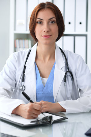 Doctor woman at work. Physician filling up medical history records form at the desk. Medicine, healthcare  conceptの写真素材