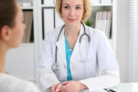Happy blonde female doctor and patient discussing medical examination results. Medicine, healthcare and help conceptの写真素材
