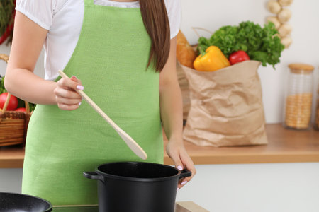 Young woman cooking with pan in kitchen, hands close-up. Householding, tasty food conceptsの写真素材