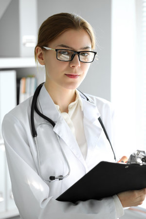 Doctor woman at work. Portrait of female physician using clipboard at hospital office. Medicine and healthcare conceptの写真素材