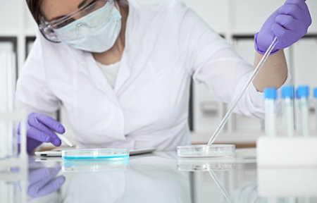 Close-up of professional female scientist in protective eyeglasses making experiment with reagents...