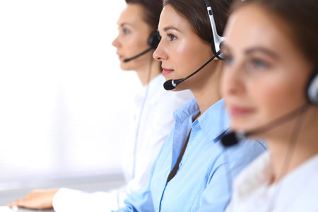 Call center. Group of operators at work. Focus at beautiful business woman in headsetの写真素材