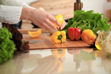 Unknown human hands cooking in kitchen. Woman slicing yellow bell pepper. Healthy meal, and vegetarian food conceptの写真素材