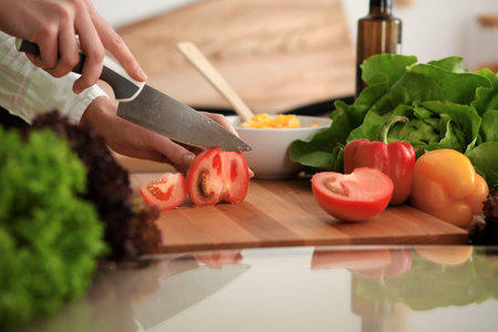 Unknown human hands cooking in kitchen. Woman slicing red tomatoes. Healthy meal, and vegetarian food conceptの写真素材