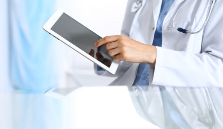 Woman doctor using tablet computer while sitting. Reflecting glass table is a working place of physician. Healthcare, insurance and medicine conceptの写真素材