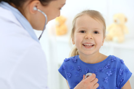 Doctor examining a little girl by stethoscope. Happy smiling child patient at usual medical inspection. Medicine and healthcare conceptsの写真素材