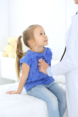 Doctor examining a little girl by stethoscope. Happy smiling child patient at usual medical inspection. Medicine and healthcare conceptsの写真素材