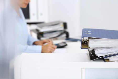 Binders with papers are waiting to be processed by business woman or bookkeeper back in blur....