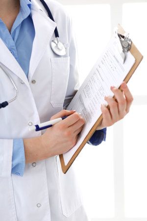 Female doctor using medical form on clipboard closeup.  Physicianat work in hospital or clinic. Healthcare, insurance and medicine concept