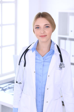 Young woman doctor at work in hospital looking at camera. Blue colored blouse of therapist looks good. Medicine and healthcare conceptの写真素材