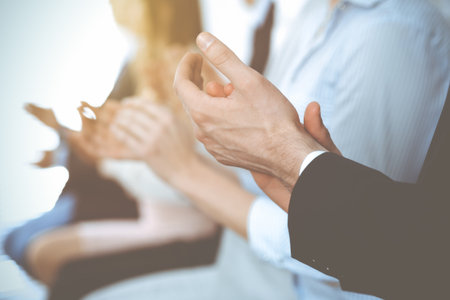 Business people clapping and applause at meeting or conference, close-up of hands. Group of unknown businessmen and women in modern white office. Success teamwork or corporate coaching concept.の写真素材