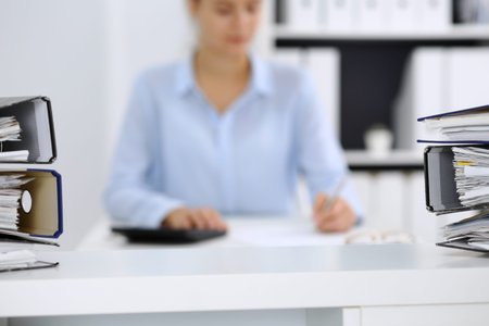 Calculator and binders with papers are waiting to be processed by business woman or bookkeeper back...