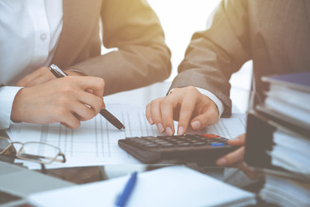 Two female accountants counting on calculator income for tax form completion hands close-up. Business and audit conceptの写真素材