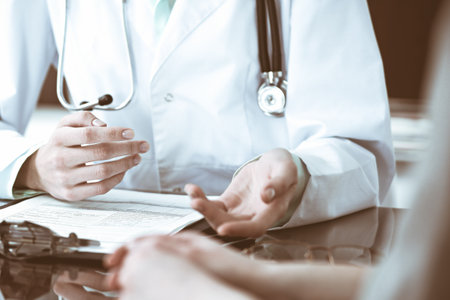 Close up of doctor and  patient  sitting at the desk near the window in hospitalの写真素材