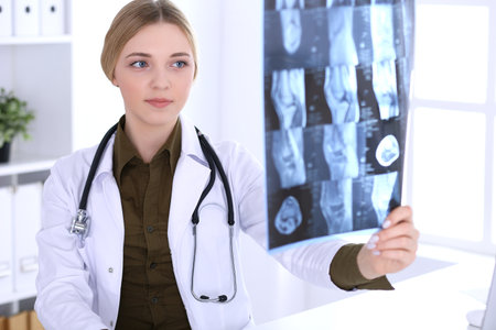 Doctor woman examining x-ray picture near window in hospital. Surgeon or orthopedist at work. Medicine and healthcare concept. Khaki colored blouse of a therapist looks goodの写真素材