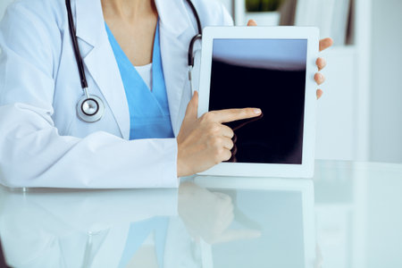 Female doctor using tablet computer while sitting at the workplace, close-up of hands. Medicine, healthcare and help conceptの写真素材