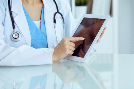 Female doctor using tablet computer while sitting at the workplace, close-up of hands. Medicine, healthcare and help conceptの写真素材