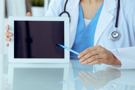 Female doctor using tablet computer while sitting at the workplace, close-up of hands. Medicine, healthcare and help concept.の写真素材