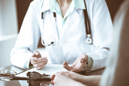 Doctor and female patient sitting at the desk and talking in clinic near window. Medicine and health care concept. Green is main colorの写真素材