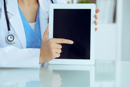 Female doctor using tablet computer while sitting at the workplace, close-up of hands. Medicine, healthcare and help conceptの写真素材