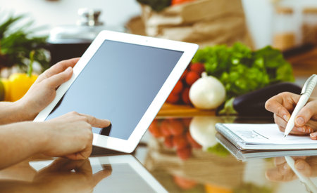 Close-up of human hands using tablet or touch pad. Two women in kitchen. Cooking, friendship or family fun conceptsの写真素材