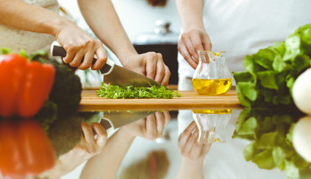 Closeup of human hands cooking in kitchen. Mother and daughter or two female friends cutting vegetables for fresh salad. Friendship, family dinner and lifestyle conceptsの写真素材