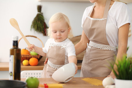 Happy mother and little daughter cooking in kitchen. Spending time all together, family fun conceptの写真素材