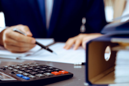 Binders with papers waiting to be processed with businessman or bookkeeper back in blur. Accounting planning budget. Audit, insurance and business conceptの写真素材