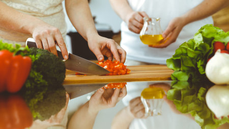 Closeup of human hands cooking in kitchen. Mother and daughter or two female friends cutting vegetables for fresh salad. Friendship, family dinner and lifestyle conceptsの写真素材