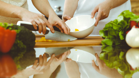 Closeup of human hands cooking in kitchen. Mother and daughter or two female friends cutting vegetables for fresh salad. Friendship, family dinner and lifestyle conceptsの写真素材
