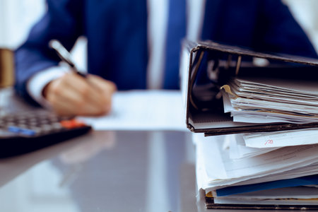 Binders with papers waiting to be processed with businessman or bookkeeper back in blur. Accounting planning budget. Audit, insurance and business conceptの写真素材