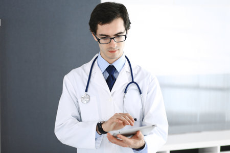 Doctor man using tablet computer for network research or virtual disease treatment. Perfect medical service in clinic. Modern medicine, medic data and healthcare conceptsの写真素材