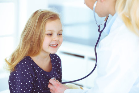 Doctor examining a child patient by stethoscope. Cute baby girl at physician appointment. Medicine...