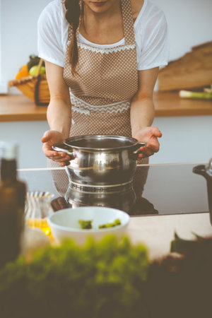 Young brunette woman cooking soup in kitchen. Food and health conceptの写真素材