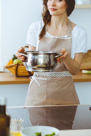 Young brunette woman cooking soup in kitchen. Food and health conceptの写真素材