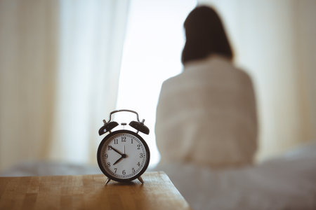 Woman stretching hands in bed after wake up, sun flare . Brunette entering a day happy and relaxed after good night sleep and back view. Concept of a new day and joyful weekendの写真素材