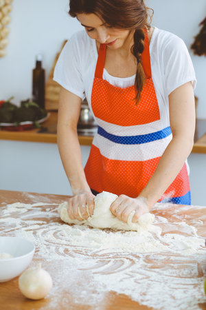 Young brunette woman cooking pizza or handmade pasta in the kitchen. Housewife preparing dough on wooden table. Dieting, food and health conceptの写真素材