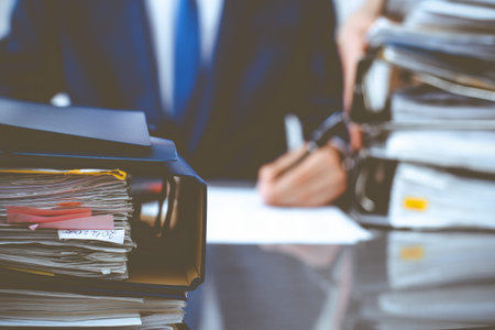 Binders with papers waiting to be processed with businessman or bookkeeper back in blur. Accounting...