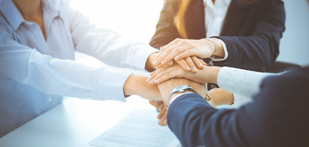 Business team showing unity with their hands together in sunny office. Group of people joining hands...