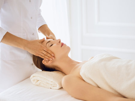 Beautiful woman enjoying facial massage with closed eyes in spa center. Relaxing treatment concept in medicine.の写真素材