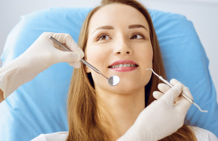 Smiling young woman with orthodontic brackets examined by dentist at dental clinic. Healthy teeth and medicine conceptの写真素材